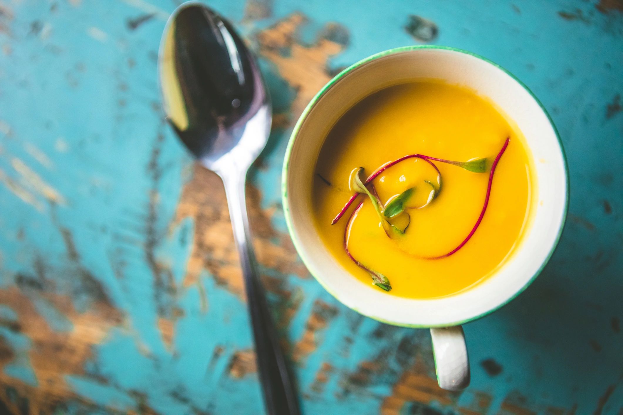 Cup of creamy yellow soup with an herb garnish.